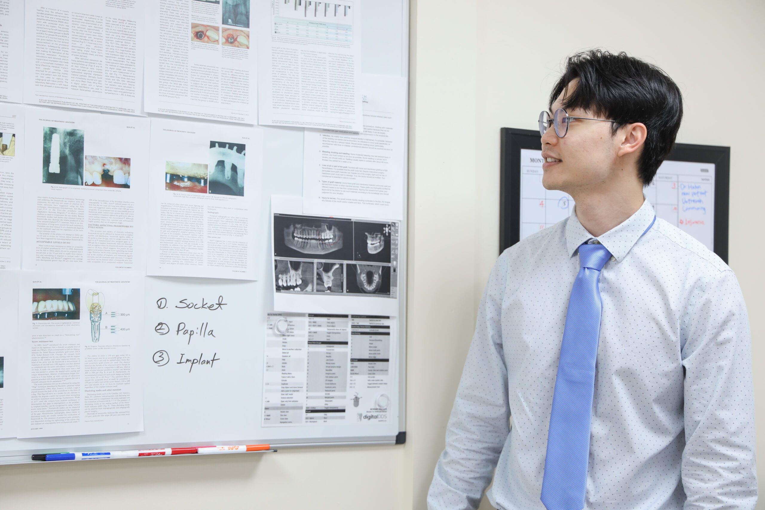 A clinician reviewing implant case notes and radiographs pinned to a board at Think Dental Institute